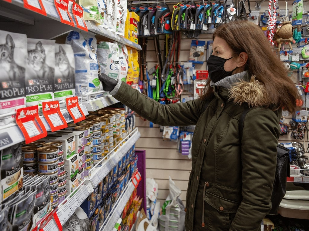 mulher de máscara escolhendo ração na prateleira do petshop
