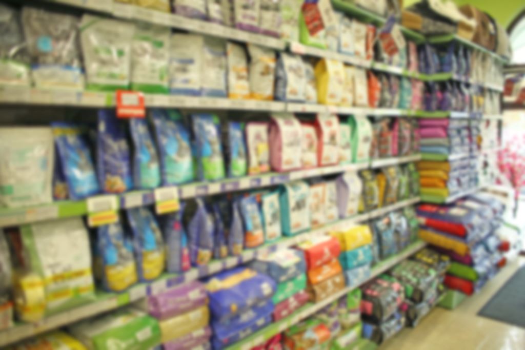 Na imagem, há uma prateleira, cheia de produtos pet. A foto está desfocada.